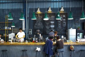 A bustling café with a modern industrial design, featuring a barista making coffee and patrons enjoying drinks.