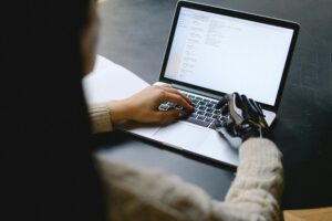 A person with a prosthetic hand using a laptop, showcasing technology and inclusivity.Future of Resume Screening: Will AI Replace Recruiters?