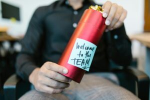 A red gift box held by a person with a welcome to the team note, ideal for new hire announcements.